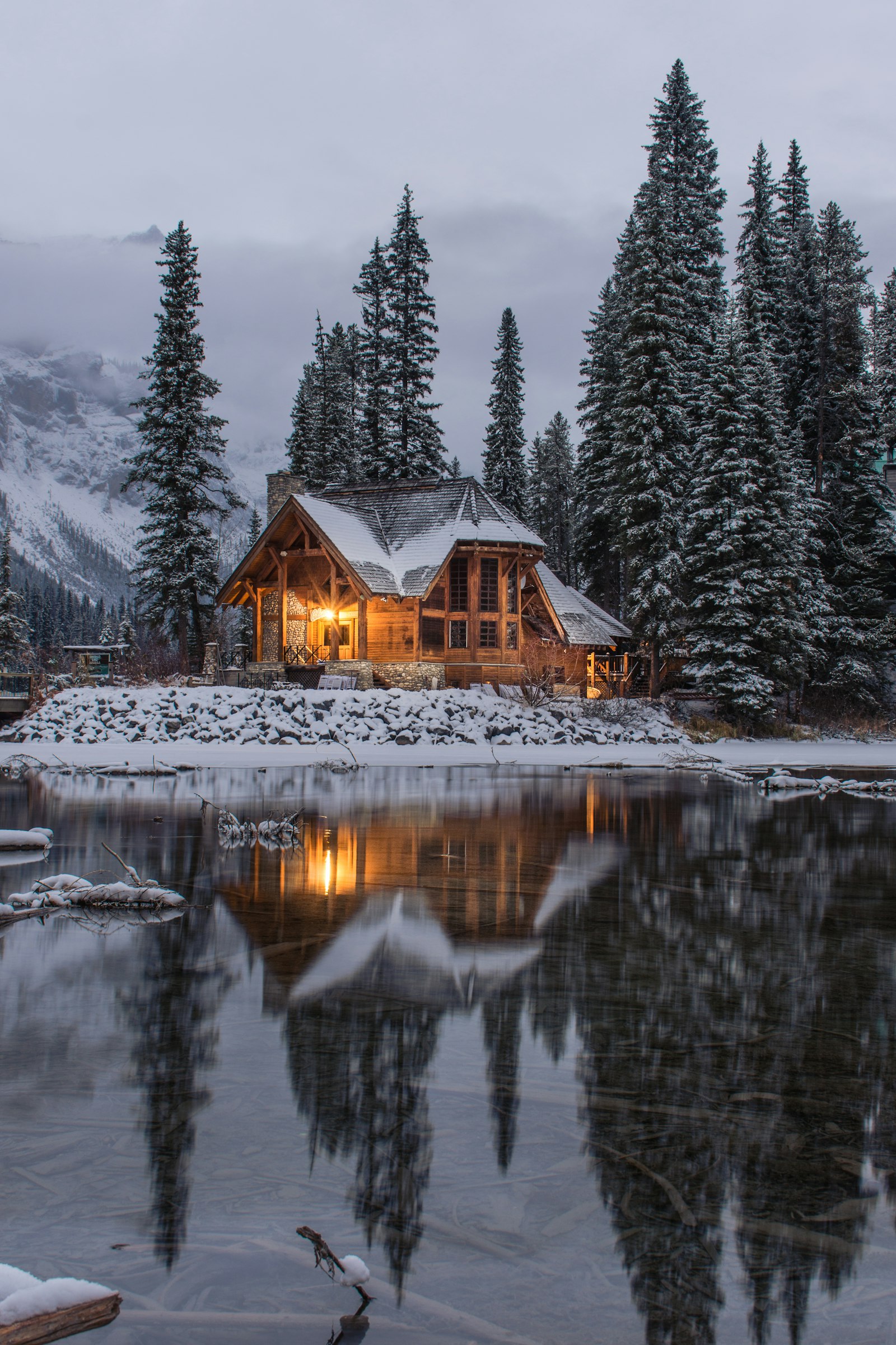 Verschneite Holzhütte am zugefrorenen Waldsee im Winter